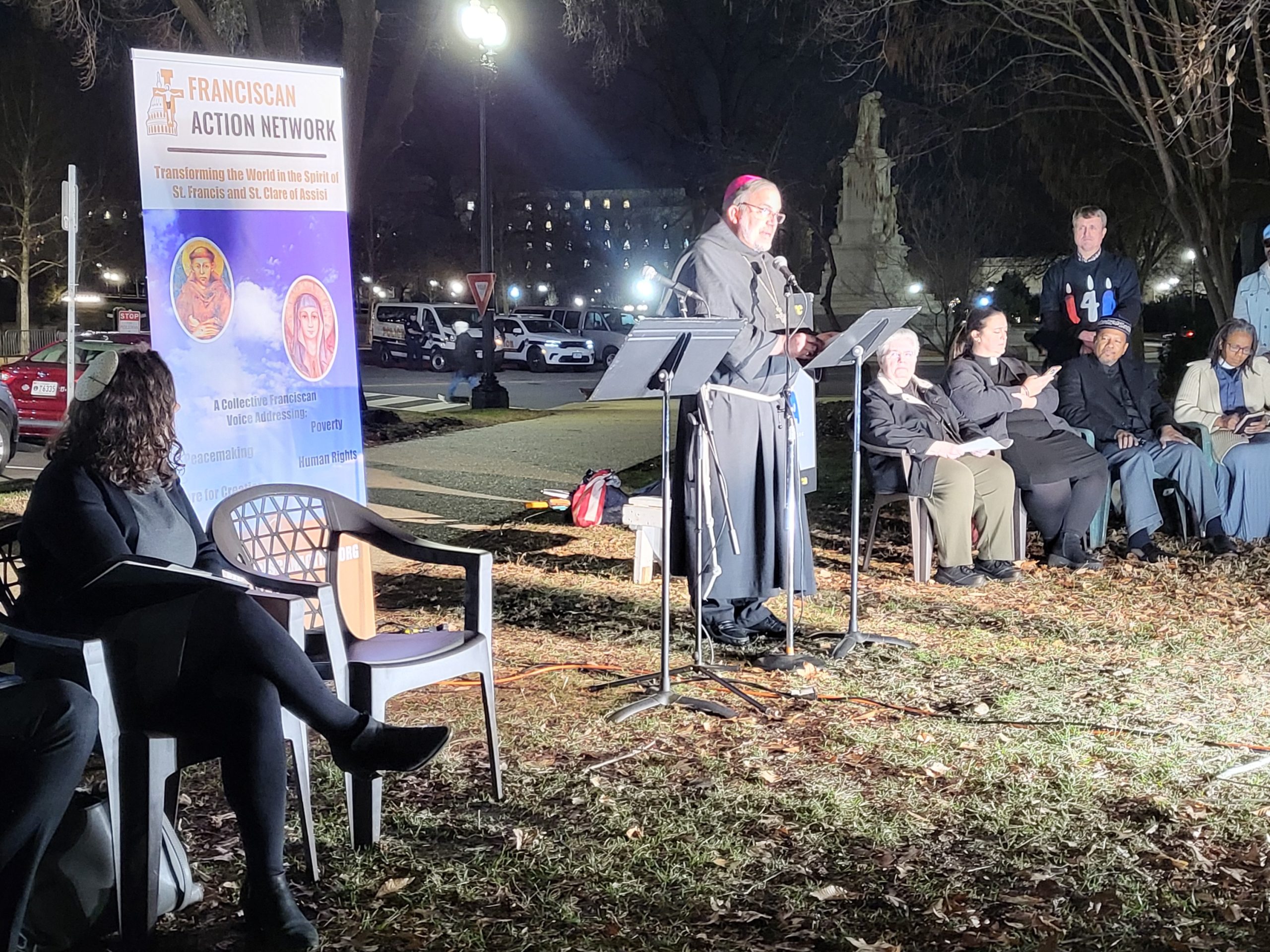 Bishop Stowe stands at the microphone while other speakers look on.