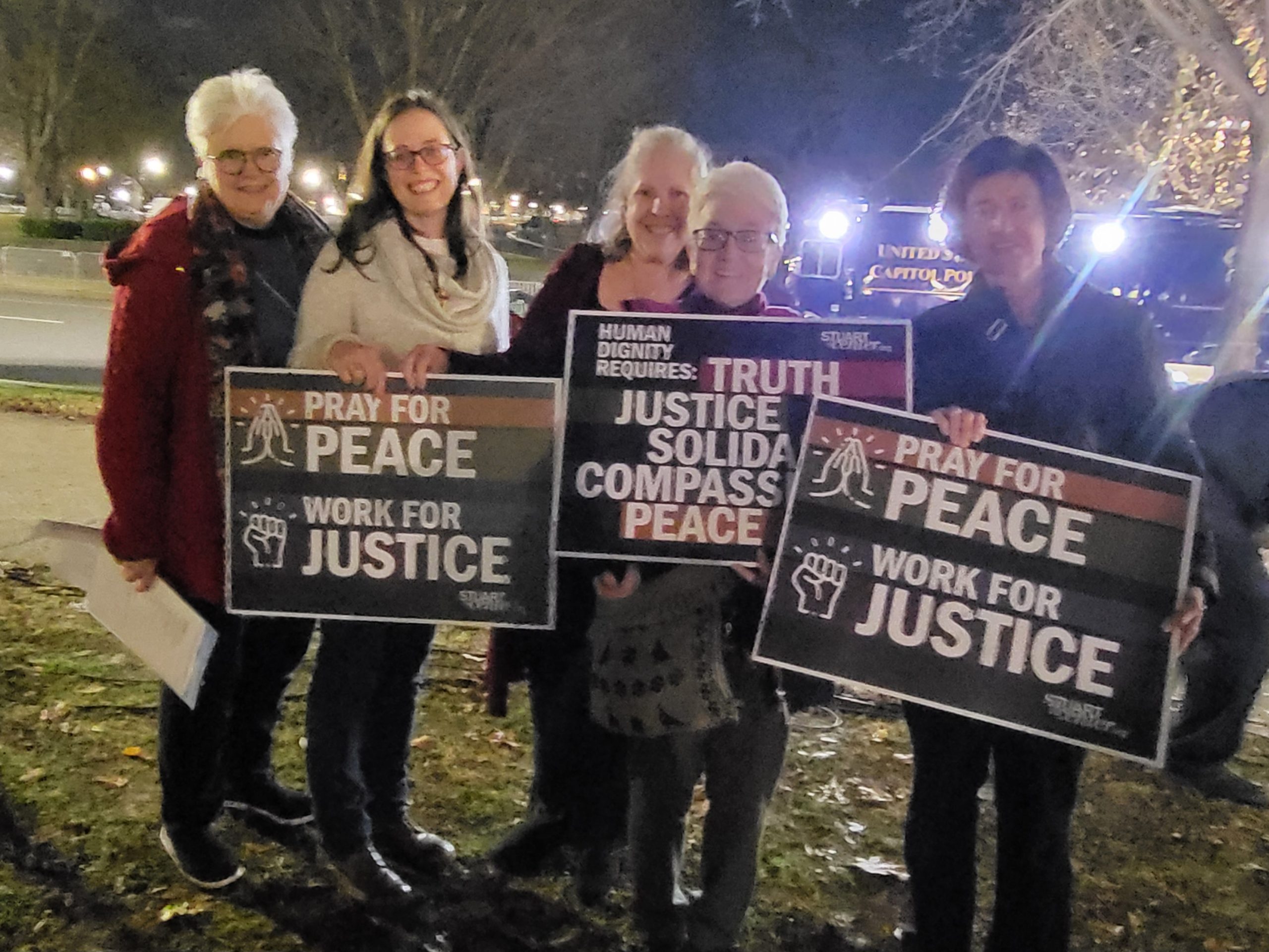 Photo of five attendees at the Jan 5 vigil holding signs that read "Pray for Peace, Work for Justice" 